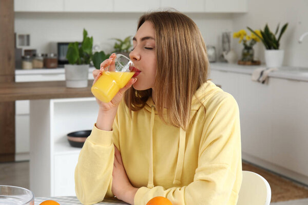 Young woman drinking orange juice in kitchen