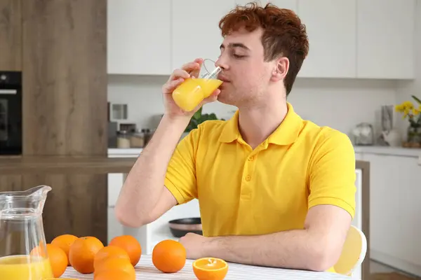 Young man drinking orange juice in kitchen