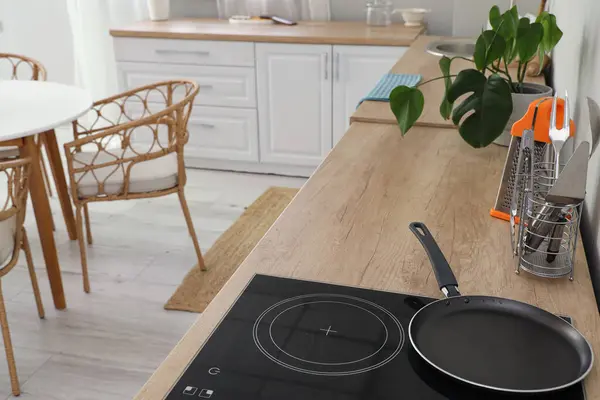 Electric stove with clean frying pan on wooden countertop in interior of light kitchen