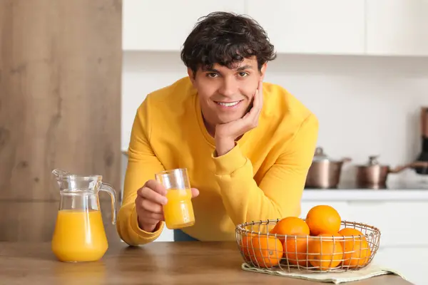 Young man with juice and oranges in kitchen