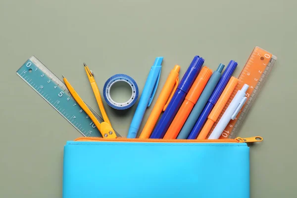 Blue pencil case with school stationery on green background