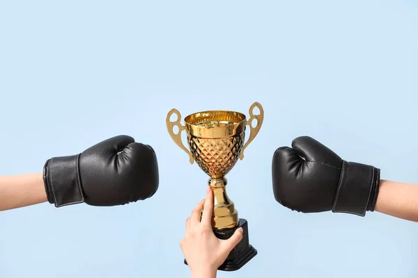 Female hands with gold cup and boxing gloves on blue background