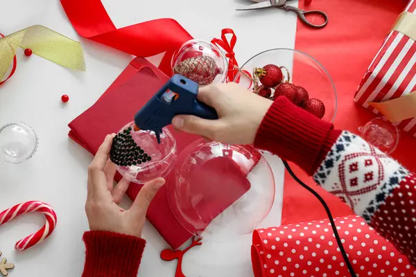 Woman holding glue gun and decorating Christmas ball with rhinestones on table