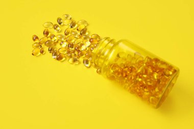 Sarı arka planda dağınık haplarla dolu kavanoz.