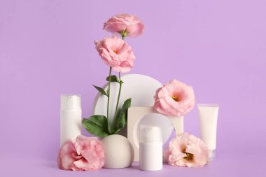 Farklı kozmetik ürünleri, alçı podyum ve mor arka planda güzel östoma çiçekleri içeren kompozisyon