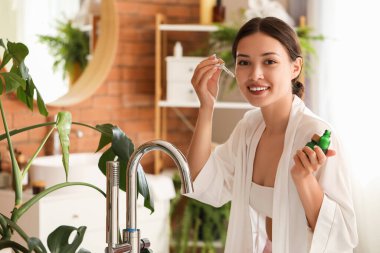 Güzel Asyalı kadın banyoda serum uyguluyor.