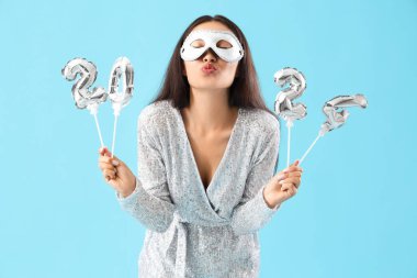 Karnaval maskesi ve 2024 model balonları olan güzel Asyalı kadın mavi arka planda.