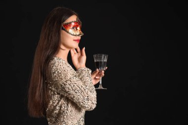 Karnaval maskeli, siyah arka planda bir bardak şarapla güzel bir Asyalı kadın.