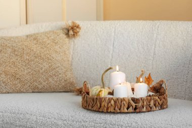 Kanepede yanan mumlar ve sonbahar dekoru olan hasır tepsi.