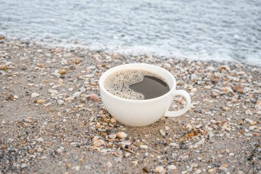 Çakıl taşlı sahilde seramik bir fincan kahve.