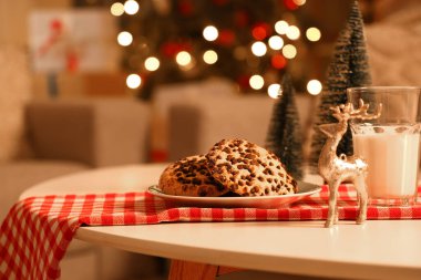 Geceleri odadaki masada bir bardak süt ve dekorlu Noel kurabiyeleri, yakın plan.