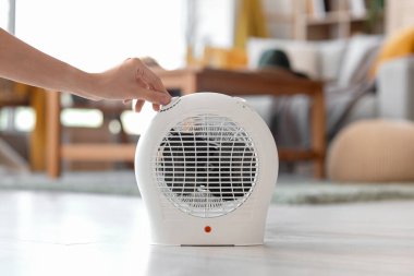 Woman turning on electric fan heater at home, closeup