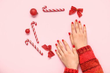 Kırmızı manikürlü kadın elleri ve pembe arka planda Noel dekoru.