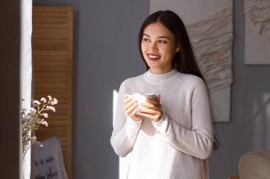 Evde bir fincan sıcak çayla genç Asyalı kadın.