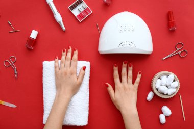 Tarz sahibi kırmızı tırnaklı kadın elleri ve renkli arka planda manikür ekipmanları.