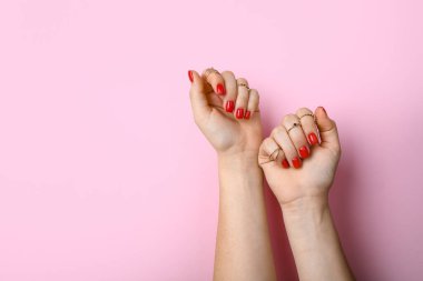 Pembe arka planda şık kırmızı manikürlü kadın elleri.