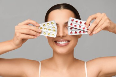Gri arka planda A vitamini kapsülleri tutan genç ve güzel bir kadın.