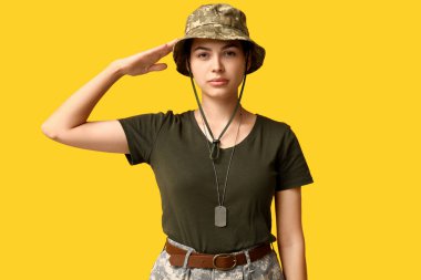 Üniformalı genç bayan asker sarı arka planda selam veriyor.