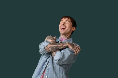 Koyu yeşil arka planda gülen genç adam.