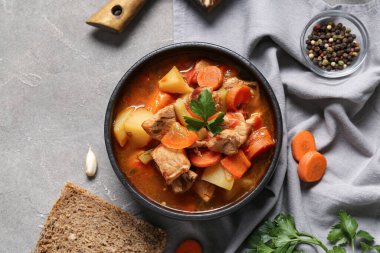 Lezzetli sığır güveci ve gri arka planda farklı malzemelerle siyah kase.