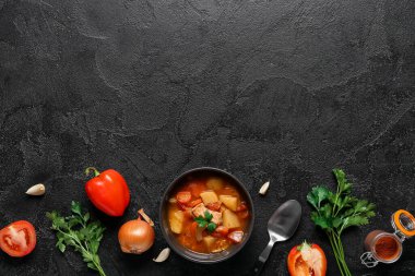 Lezzetli sığır güveci ve siyah arka planda farklı malzemelerle dolu bir kase.