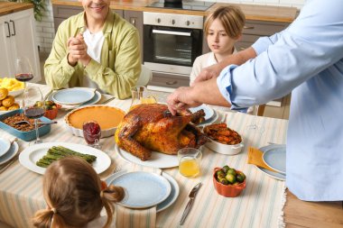 Olgun bir adam Şükran Günü 'nde ailesiyle birlikte ziyafet masasında hindi kesiyor.