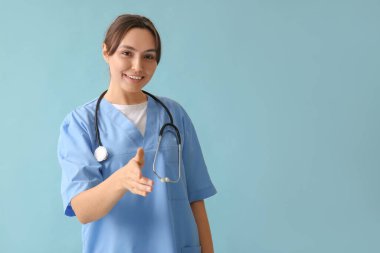 Güzel bayan doktor mavi arka planda el sıkışmak için elini uzatıyor.