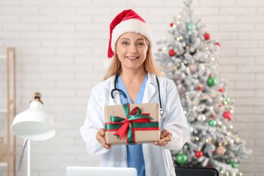 Noel Baba şapkalı olgun bir kadın doktor ve klinikte Noel hediyesi kutusu var.