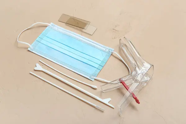 Gynecological speculum, medical mask and pap smear test tools on beige background