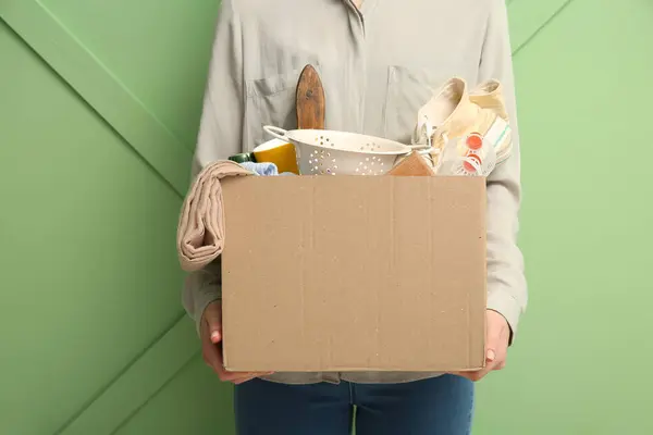Woman holding box of unwanted stuff for yard sale on green background