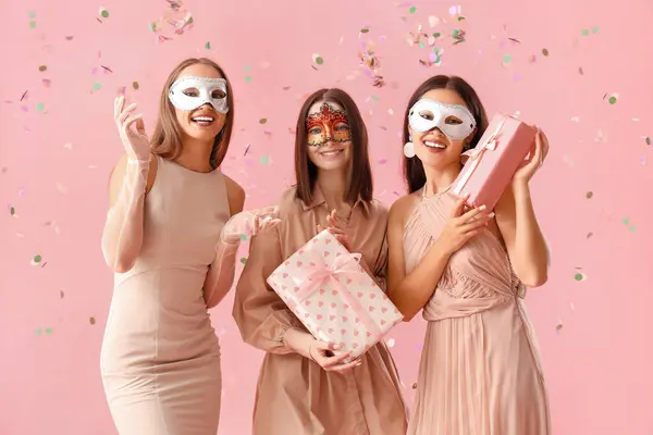 Красивые Молодые Женщины Карнавальных Масках Подарочными Коробками Розовом Фоне — стоковое фото