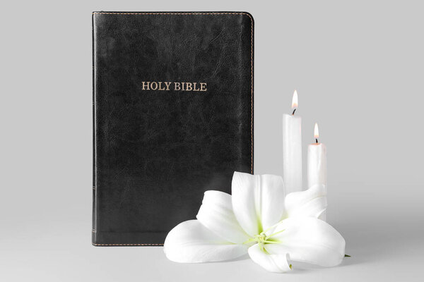 Beautiful lily flower, burning candles and Holy Bible on grey background