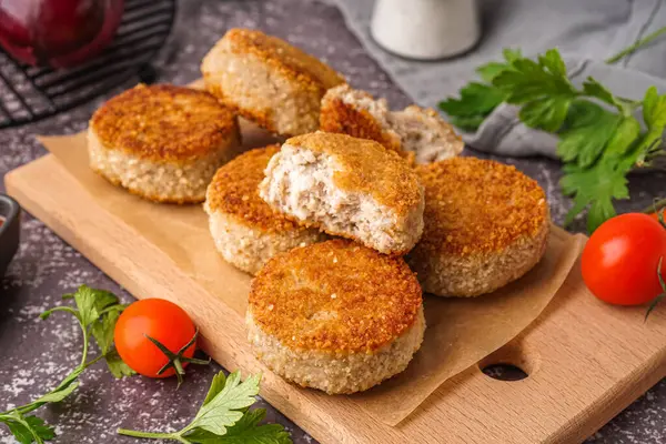 stock image Wooden board of tasty meat cutlets on grey background