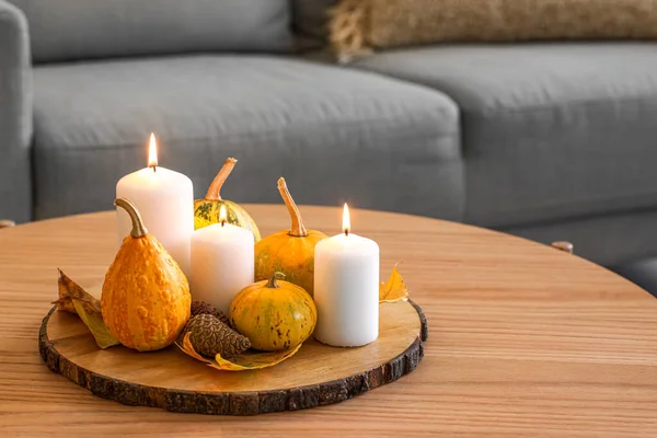 Board with burning candles and autumn decor on wooden table in room