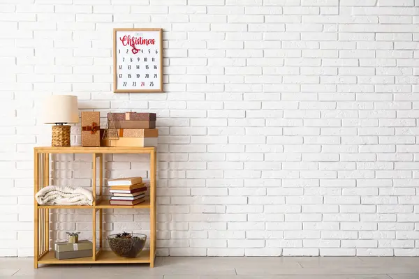 Shelf unit with presents, books and Christmas calendar on white brick wall in room
