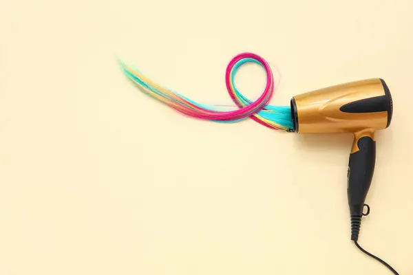 Hair dryer and colorful strands on beige background, top view