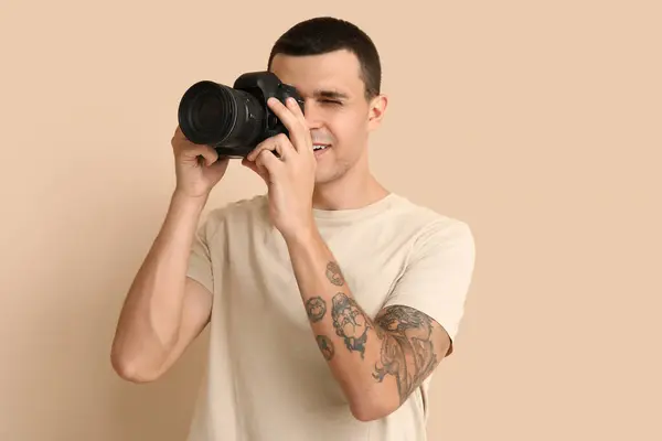 Male tattooed photographer with modern camera on beige background