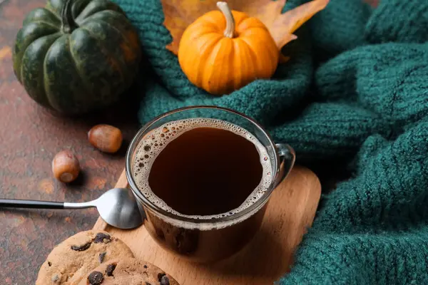 Cup of aromatic coffee, pumpkins and clothes on grunge background, closeup