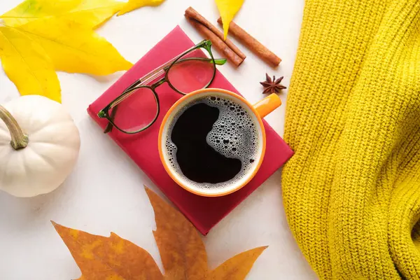 Composition with cup of aromatic coffee, book and autumn decor on light background