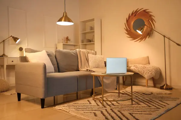 Interior of cozy living room with sofa and laptop on table in evening