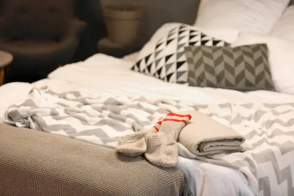 Warm socks with blankets on bed in dark bedroom, closeup