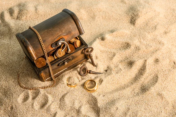 Old chest with treasures and keys on sand