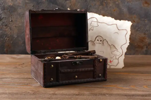 Old chest with jewelry and treasure map on brown wooden background