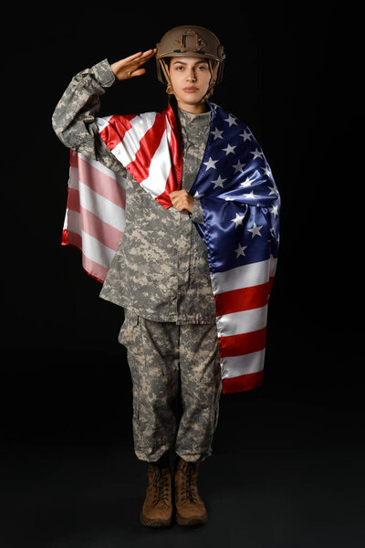 Young female soldier in uniform with flag of USA saluting on black background
