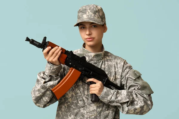 Confident young female soldier with assault rifle on blue background