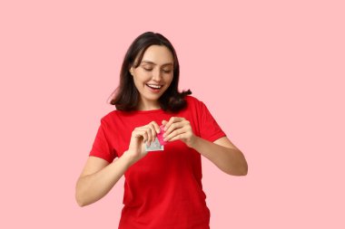 Pembe arka planda prezervatifli genç bir kadın. Güvenli seks konsepti