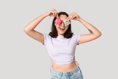 Gri arka planda prezervatifleri olan komik bir genç kadın. Güvenli seks konsepti