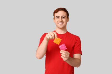 Gri arka planda prezervatifli genç bir adam. Güvenli seks konsepti