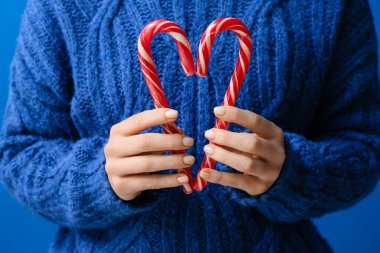 Mavi arka planda Noel şekerleri tutan bir kadın.