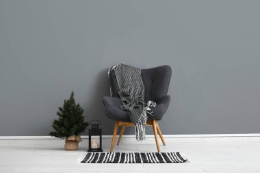 Battaniyeli modern koltuk, Noel ağacı ve gri duvarın yanındaki fener.